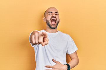 Young bald man wearing casual white t shirt laughing at you, pointing finger to the camera with hand over body, shame expression