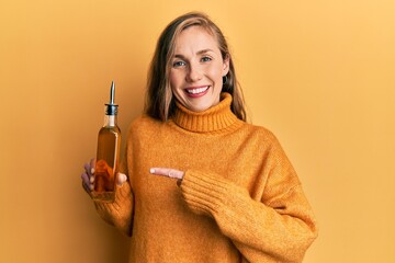 Young blonde woman holding olive oil can smiling happy pointing with hand and finger
