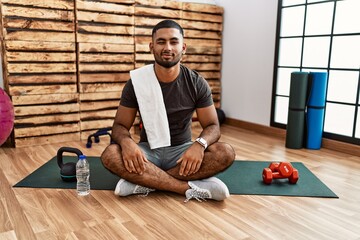 Young indian man sitting on training mat at the gym winking looking at the camera with sexy...