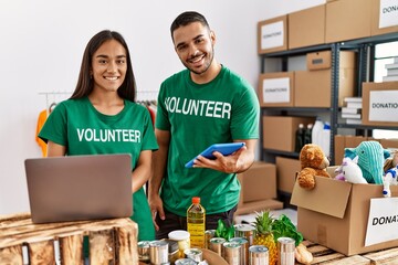 Young latin volunteer couple using laptop and touchpad working at charity center.