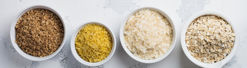 Variety of cereal flakes rice, millet, buckwheat, oatmeal. Superfood in white ceramic bowls on light wooden background. Top view.