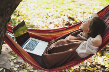 Young relaxed happy woman freelancer with laptop lying in hammock at backyard of country house on...