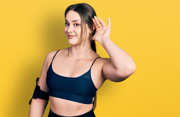 Obraz premium Young hispanic woman wearing sportswear smiling with hand over ear listening an hearing to rumor or gossip. deafness concept.