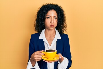 Young latin girl wearing business style drinking cup of coffee puffing cheeks with funny face. mouth inflated with air, catching air.