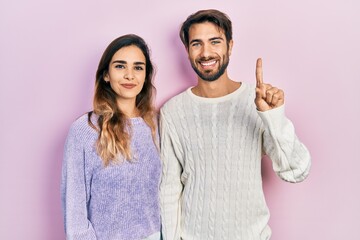Young hispanic couple wearing casual clothes showing and pointing up with finger number one while smiling confident and happy.