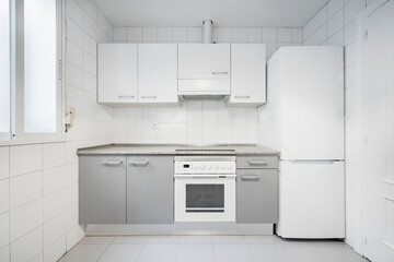 Fototapeta premium Front view of gray and white kitchen cabinets with white granite countertops, oven, refrigerator and extractor hood in a vacation rental apartment
