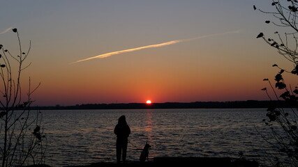 Fototapeta premium White mongrel dog and a girl greet the sunrise by the lake