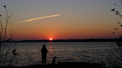 White mongrel dog and a girl greet the sunrise by the lake