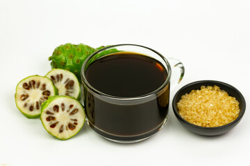 Noni juice in transparent glass cup and fresh noni fruit isolated on white background.