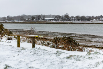 A snow covered bench along a popular countryside walk that runs along side the River Deben in the Suffolk countryside
