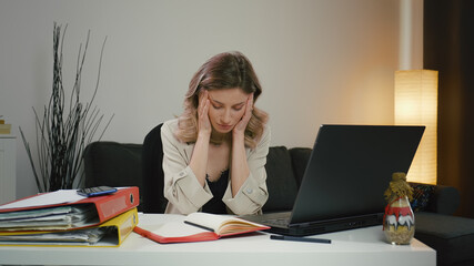 Tired woman, overwhelmed by laptop work, has severe headache.