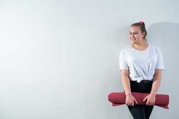 Obraz premium Young fat caucasian woman holding a sport mat. Charming plus size model in sportswear stands on a white background