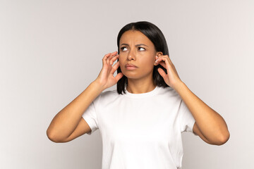 Irritated young woman plugging ears in stressed with sudden noise from neighbor look up with annoyed and displeased face expression. African american female dissatisfied with noisy sound cover head