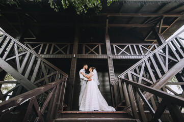 Beautiful, stylish newlyweds stand, hug against the background of a large wooden house on the...