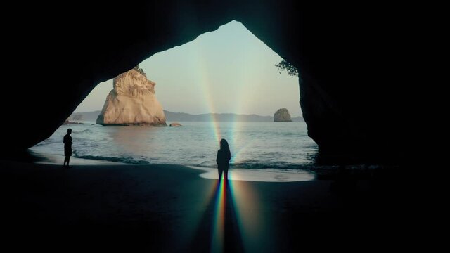 Aerial: Woman with light ray aura looking out of a cave. Cathedral cove, New Zealand