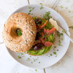plate with bagel with cream cheese, avocado, salmon and kalamata olives on a light table