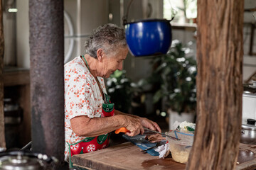 Mujer adulta mayor cortando en la cocina antigua de su casa de madera