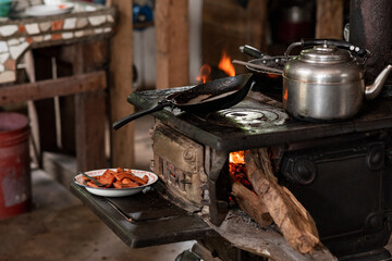 Estufa antigua de metal encendida con leña con un sarten cocinando embutidos