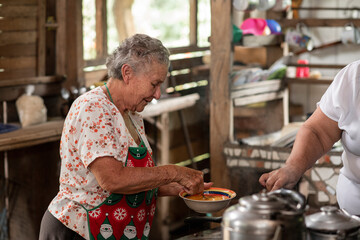 Mujer adulta mayor cocinando en una estufa metálica con leña en su casa de madera 
