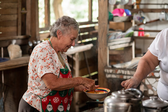Mujer adulta mayor cocinando en una estufa met&aacute;lica con le&ntilde;a en su casa de madera 