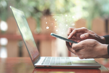 social media symbols, Communication via the Internet and applications concept. Man hands holding smartphone and touching screen with laptop on wooden desk, Virtual images media icons in living room