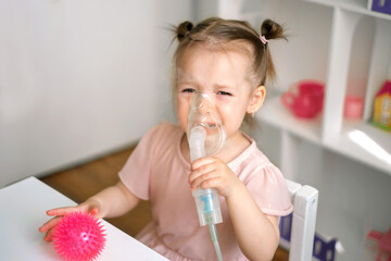 A baby holds a breathing mask and cries while Inhalations. Children's viral diseases. Inhalations for runny nose, respiratory diseases and астме. Children's nebulizer for inhalation. - obrazy, fototapety, plakaty