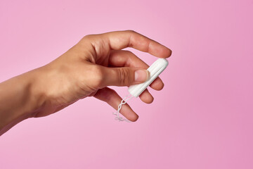 hygienic tampon in a female hand on a pink background