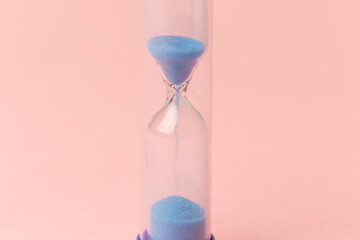 Modern blue Hourglass on pink background. Sand trickling through the bulbs of a crystal sand glass. Symbol of time. Countdown. Copy space. Top view. Concept