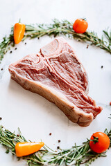 raw t-bone steak in the center of a Christmas wreath of rosemary thyme cherry tomatoes and bell peppers on a white marble surface. christmas dinner concept