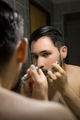 Hombre afeitándose con afeitadora clásica en el baño de su casa