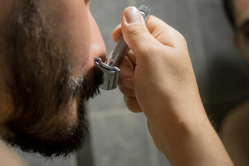 Hombre afeitándose con afeitadora clásica en el baño de su casa