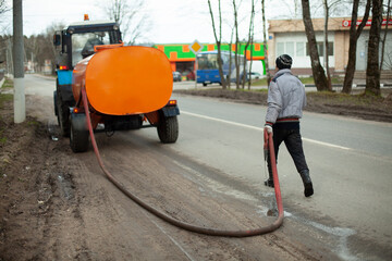 A man washes the road. Worker with a hose for water supply. Special city service in Russia....