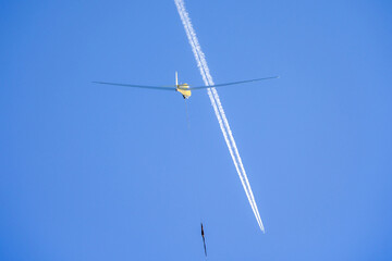 a glider is pulled into the sky with condensation stripes in background