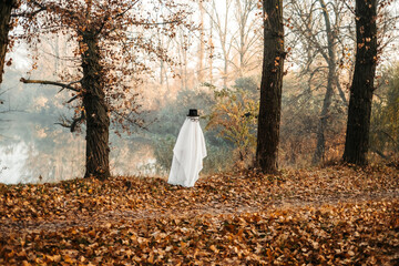 A ghost covered with a white ghostly leaf wearing a hat in the forest for Halloween. Halloween concept