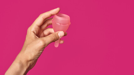 silicone pink hygienic menstrual cup in female hand on pink background