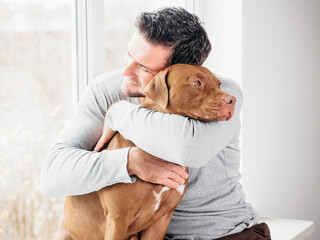Adorable man and lovable, pretty puppy of brown color. Close-up, indoor. Day light. Concept of...