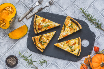 Pieces of pumpkin tart with rosemary on a slate plate on gray background, top view