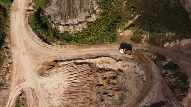 A dump truck is driving on the road in a sandy quarry for loading. Top view from quadcopter to mooving car at sand pit. Drone view and rotation with camera down at sunny day