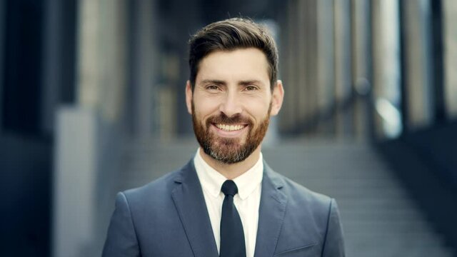 close up portrait happy Bearded Caucasian business man looking at camera outside. Face of smile handsome successful businessman in formal suit on modern urban city street background outdoor closeup