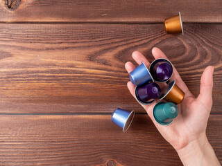 a hand hold a handful of colorful coffee capsules over a brown wooden background. Top view, copy...