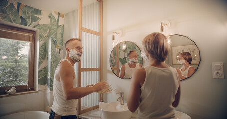 Father teaching his little son how to shave in the bathroom at home. Having fun together, looking at mirror reflections
