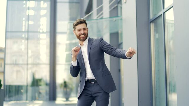 Cheerful happy business man dancing walk the city ​​street background a modern office building outside, outdoors Funny successful businessman in suit rejoices joyfully jump celebrates victory, success