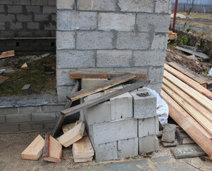 an unfinished wall of a building made of gray concrete stone, stacked bricks and boards near the house in the garden in autumn