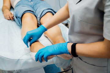 A master or cosmetologist in blue gloves rubs the client's feet, preparing for the epilation procedure.