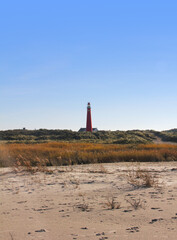 
One of Schiermonnikoog's (the Netherlands) lighthouses, the Noordertoren, seen from the beach. This tower is bright red. You can see a bit of the sand and the dunes. Clear sky. 
