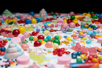 Candy in variety of colour, shape, size and flavours mixed on the table with real white sugar. International Candy Day background. Sweet stock of snack, chocolates, caramels, candy, and jelly beans.