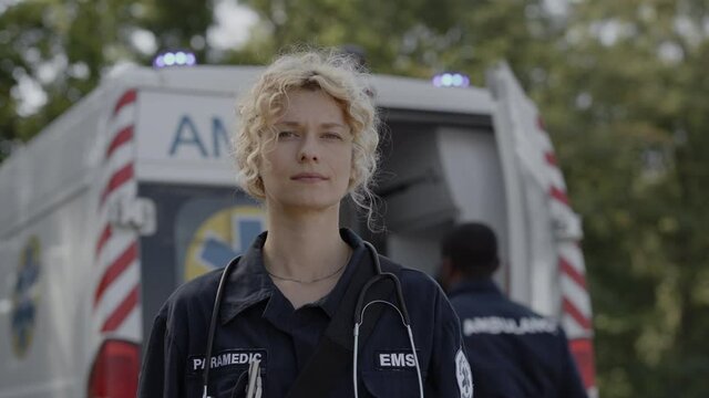 Female paramedic standing on street with ambulance behind