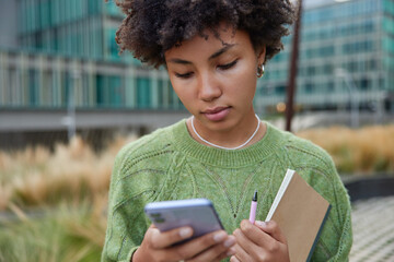 Cropped image of serious female model concentrated at screen of smartphone reads information online...