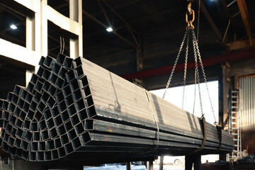 The hook of an electric crane lifts a steel bar into the air at the factory. Loading a metal...