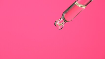 Oil or liquid dropper or pipette in extreme macro close up. Drop of yellow cosmetic lavender oil falling on pink background. Eyedropper squeezing out meds droplets.